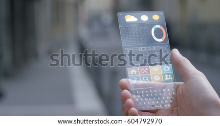 A man in the city, use the transparent phone with the latest technology with holography and watch the weather and the messages. Concept: technology, future and futuristic technology. Royalty-Free Stock Photo #604792970