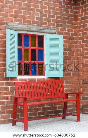 Red bench in front of the green window with the brick wall
