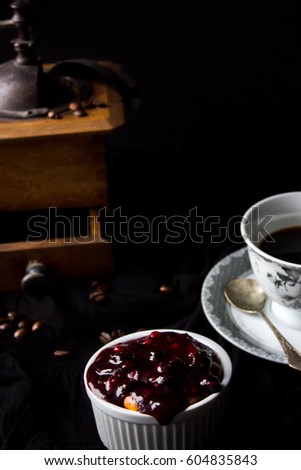 dessert- cheesecake in ramekin with forest fruit and gelatine. in the background cup of coffee and old-fashioned coffee grinder. dark picture, moody photography, low key. 