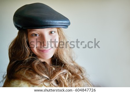 Little beautiful smiling girl in warm fur coat and black leather cap close up.