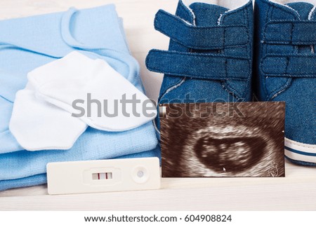 Pregnancy test with positive result, ultrasound scan of baby and clothing for newborn on boards, concept of extending family and expecting for baby