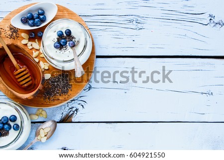 Mason jars of healthy yogurt with chia seeds, honey and fresh blueberries for breakfast on white grunge wooden background, top view, copy space. Detox, dieting, vegan, vegetarian, clean eating concept