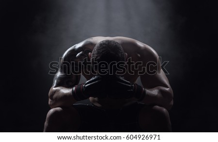 Boxer athlete sits with a drooping head on a black background Royalty-Free Stock Photo #604926971
