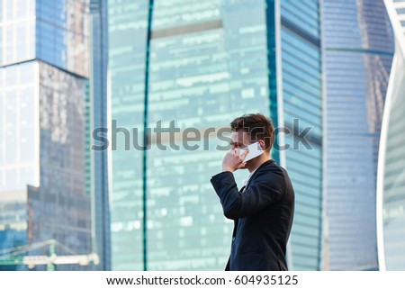 Man in suit talking on mobile phone on background of skyscrapers with glass facade