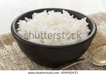 boiled rice in black bowl in wooden background