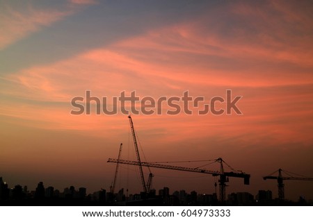 Silhouette of buildings and construction cranes against twilight pastel orange and blue sky 