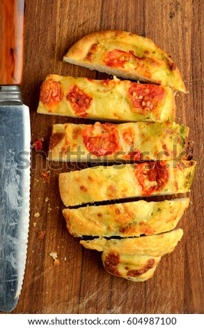 Pesto cheesy focaccia bread with tomato fresh from oven on wooden cutting board.