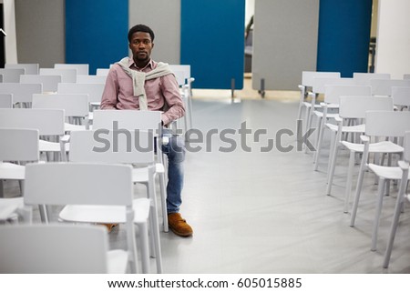 Serious student sitting on chair in empty conference-hall