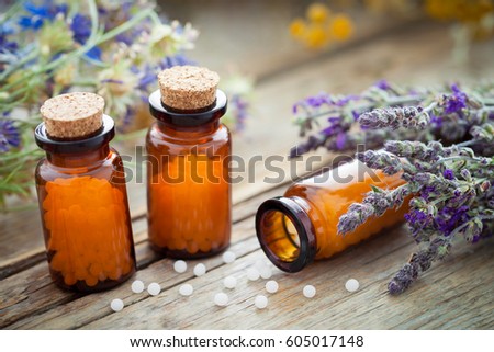 Bottles of homeopathic globules and healing herbs on wooden board. Homeopathy medicine.