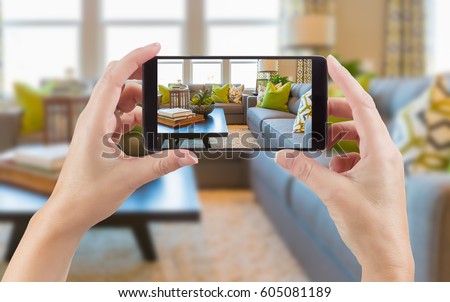 Female Hands Holding Smart Phone Displaying Photo of House Interior Living Room Behind.