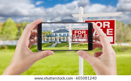 Female Hands Holding Smart Phone Displaying Photo of For Sale Real Estate Sign and House Behind.