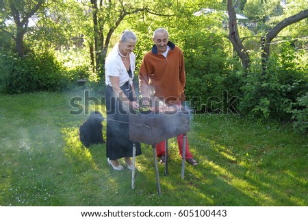 Senior man and woman frying meet in summer garden. Elderly wife and husband, black dog
