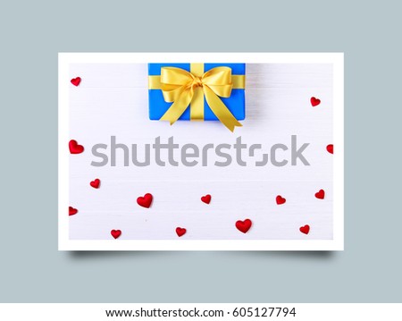 Gift box with red satin hearts. Present wrapped with yellow ribbon. Christmas or birthday blue package. On white wooden table. Photo frame design with shadow.