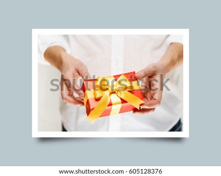 Male hands holding a gift box. Present wrapped with ribbon and bow. Christmas or birthday red package. Man in white shirt. Photo frame design with shadow.