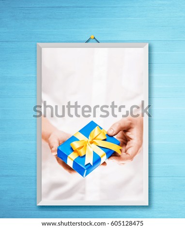 Male hands holding a gift box. Present wrapped with ribbon and bow. Christmas or birthday blue package. Man in white shirt. Photo frame on wooden rustic wall.