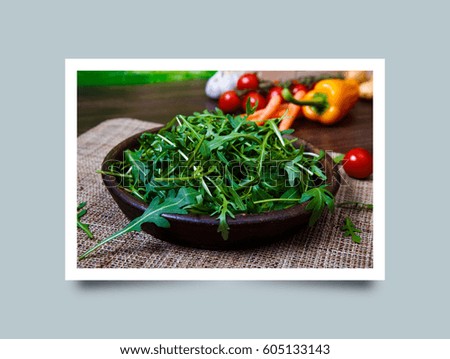 Arugula leaves in bowl. Fresh salad. Pepper and cherry tomatoes. Natural raw vegetables. Organic bio food on rustic wooden table. Photo frame design with shadow.