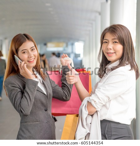 Young business woman with shopping bags showing thumbs up. Happy Asian girl talking on her smart phone in shopping mall, copy space.