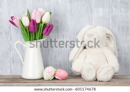 Rabbit toy, easter eggs and colorful tulips bouquet in front of wooden wall