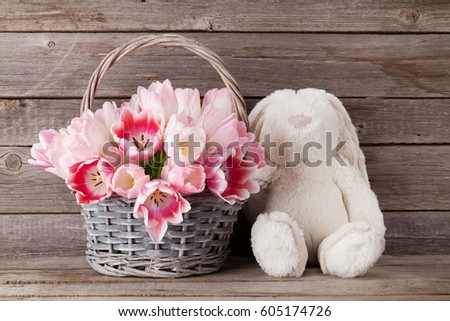 Pink tulips bouquet basket and rabbit toy in front of wooden wall. Easter greeting card