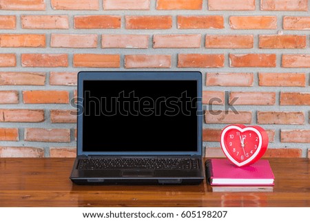 Mock up Black Blank Screen Laptop with clock on wood table in outdoor place brick wall.