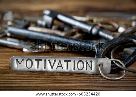Photo of key bunch on wooden board and tag with letters imprinted on clean metal surface; concept of MOTIVATION
