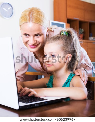 Positive nanny and girl with headset playing computer game in home interior