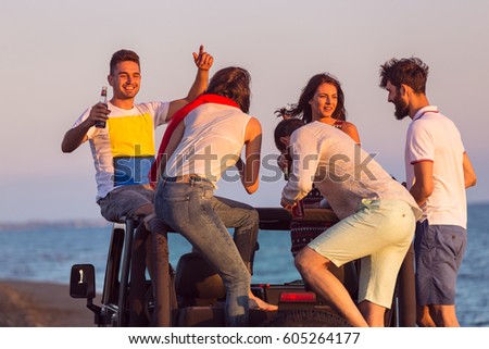 young group having fun on the beach and dancing in a convertible car