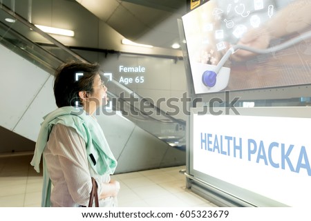 Intelligent Digital Signage marketing and face recognition concept. Old woman watch artificial intelligence digital advertisement about healthcare package in shopping Mall.