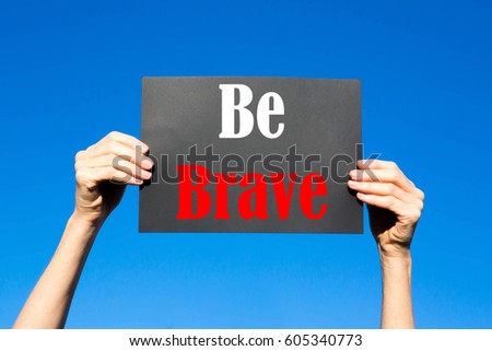 Black card placard with the concept of Be Brave against a clear blue sky background