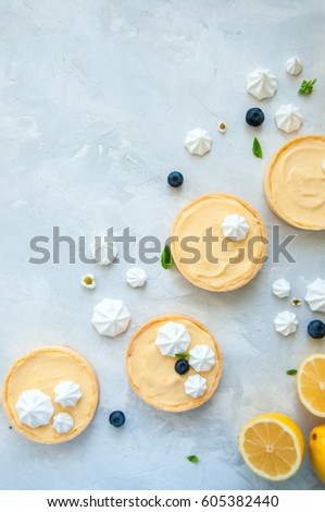 Lemon curd and blueberry jam tarts with meringue and basil leaves Chamomiles whole and slices of fresh lemon on a white stone background. Copy Space. Flat lay. Top View.