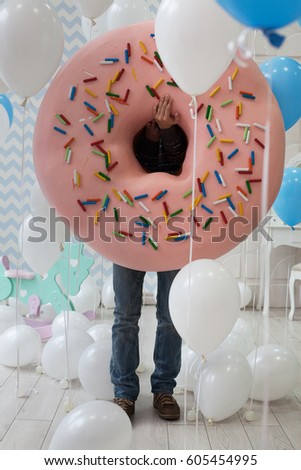 Children's animator. The child's birthday. Man is surrounded by balloons holds a huge toy doughnut.