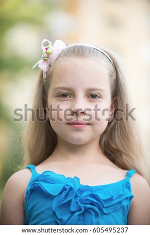 small baby girl or cute child with adorable smiling face and bow in blonde hair in blue vest outdoor on blurred background