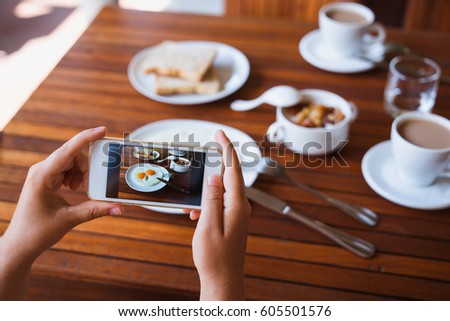 Hands of a girl with a phone smartphone make a photo of food. Breakfast of two fried eggs, coffee and oatmeal with milk.