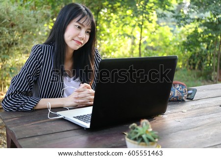 Beautiful tan skin Asian business chic woman hand typing laptop computer keyboard and phone working email with internet communication in forest. Presenting your product in coffee shop.