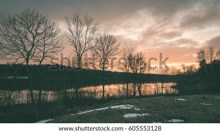 sunset over the river Daugava with dramatic colorful sky and tree silhouettes - vintage green retro effect