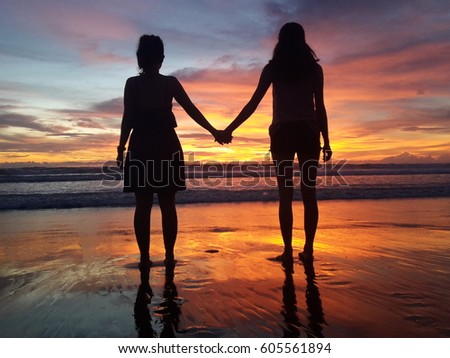 Silhouette of two friends watching sunset and holding hands in Bali, Indonesia. Best Friends holding hands.