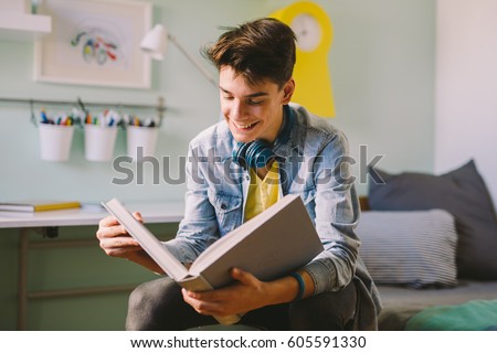 Teenage boy reading book in his room. Royalty-Free Stock Photo #605591330