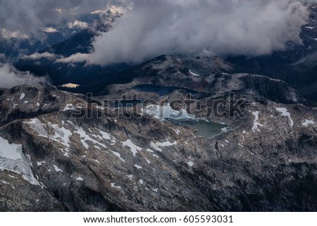 Aerial landscape view on Sigurd Peak and a Glacier Lake covered in clouds during sunset. Picture taken near Squamish, BC, Canada.