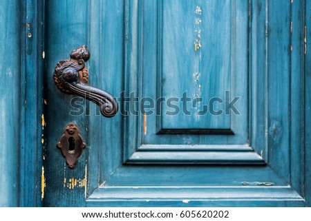 Old worn blue painted entrance door with black wrought iron latch close up image as background
