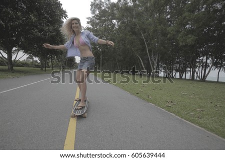 Young blonde woman skateboarding down road