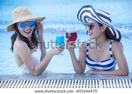 TWO woman relaxing in resort swimming pool, drinking cocktails.