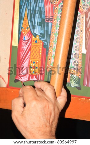 Elderly priest's hand painting an icon in the monastery's studio