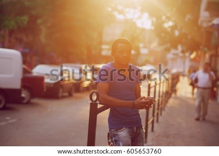Black guy walking in summer city and holding a phone