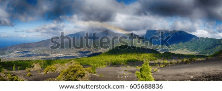 Grey clouds over volcano landscape with rainbow over green hills