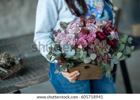 Woman florist in blue pants holds a bouquet of flowers hands in a wooden box