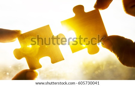 two hands trying to connect couple puzzle piece with sunset background. copy space. Jigsaw wooden puzzle against sun rays. one part of whole. symbol of association and connection. business strategy. 