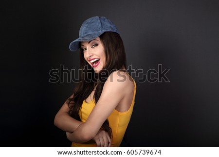 Beautiful casual joyful woman in blue baseball cap and yellow top looking with folded arms on grey background with empty copy space. Closeup portrait