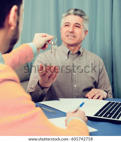 Mature man and young agent sign contract of rent apartments and hand over keys