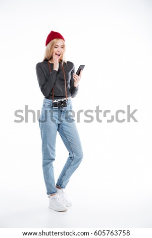 Full length of a young excited woman photographer looking at mobile phone isolated over white background