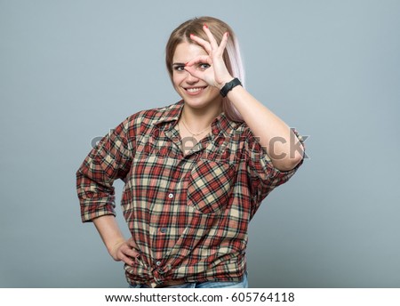 Adorable young girl look through ok sign on grey background